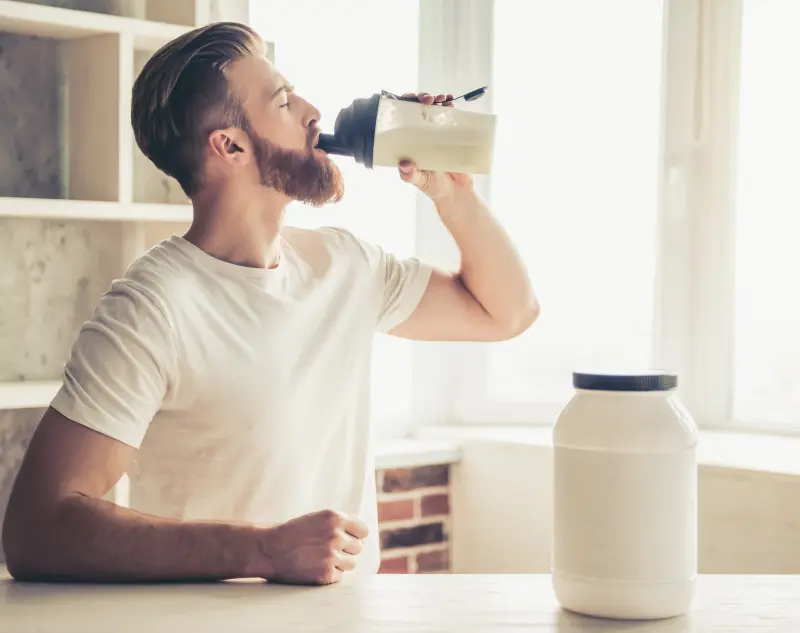 Homme qui boit un shake protéiné dans sa cuisine